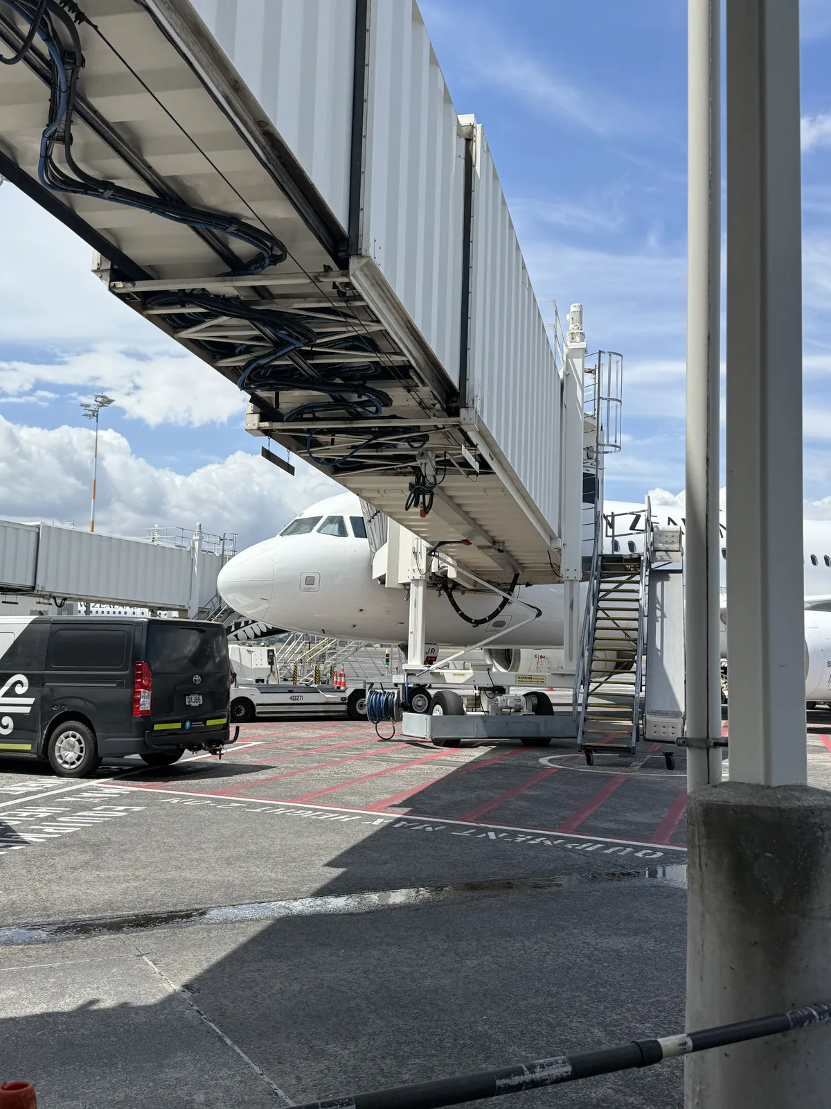 Air New Zealand aircraft at gate with passengers boarding via stairs
