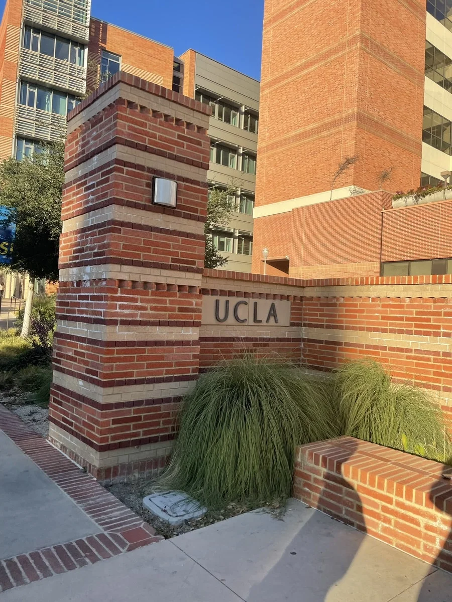 클래식한 붉은 벽돌 기둥에 새겨진 UCLA 상징 입구 표지판